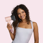 Woman holding a pink hair dryer against a light pink background