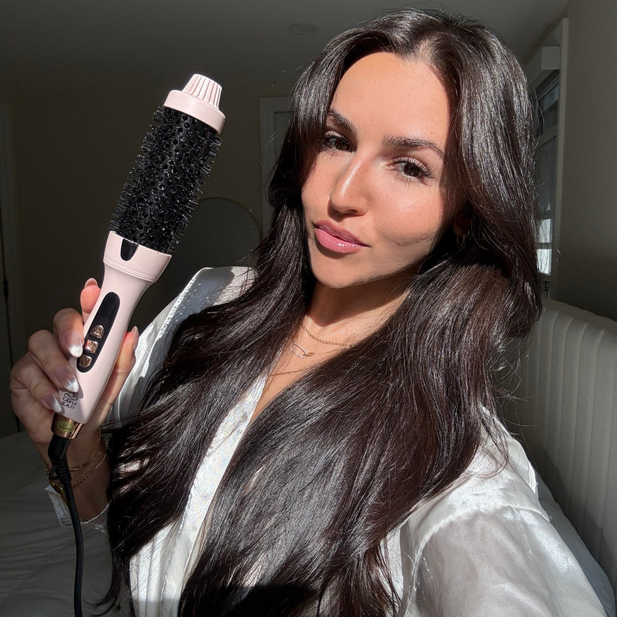 Woman holding a hair styling tool with long dark hair indoors.