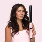 Woman holding a pink and black hair straightener against a light pink background